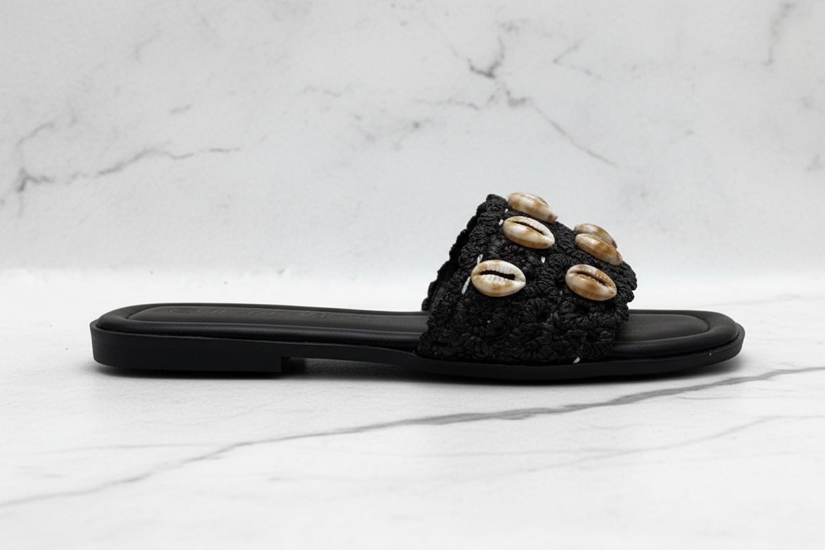 Evani Black Cowrie Shell Raffia Flat Slide Sandals – side profile view on white marble
