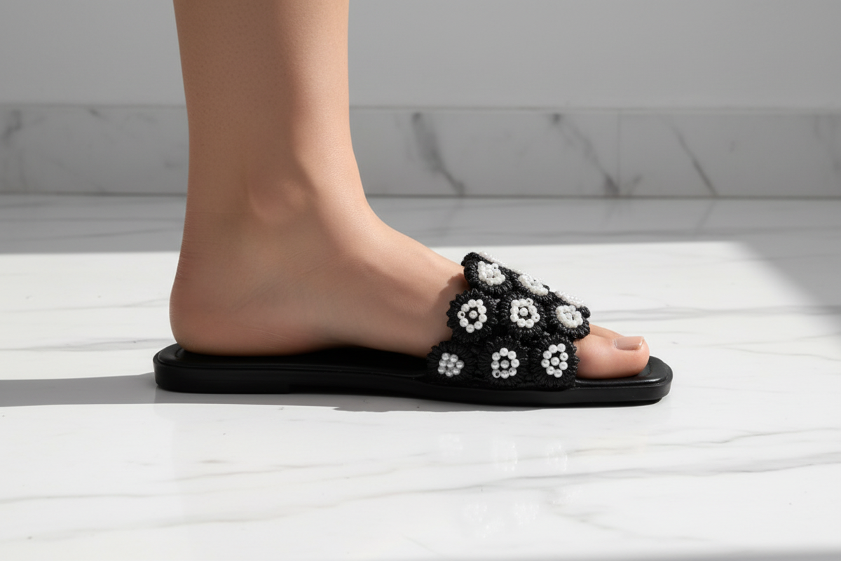 Tavo Black Pearl Flower Flat Slide Sandals – ground level profile hero shot showing 3D pearl flower rosette detail mid-stride